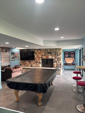 Een biljart, een stenen openhaard en een basketbalveld in een kamer met een stenen muur en blauwe wanden.