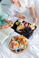 Bandeja de desayuno con tostadas, huevos, salchichas y un libro sobre la cama.