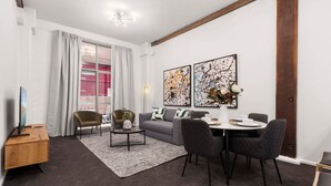 A modern living room with a grey sofa, a dining table with chairs, a wooden cabinet, and two abstract paintings on the wall. - 1 BR Apartment In the Heart of Darling Harbour (Pyrmont)