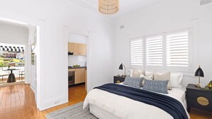 Un dormitorio con una cama grande, mesitas de noche, una ventana con persianas y vistas a la cocina y al área exterior.
