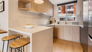 Eine moderne Küche mit Holzausbau, einer weißen Arbeitsplatte, einer eingebauten Kochinsel mit Hockern und einem Edelstahlkühlschrank.
