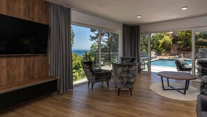 A modern living room with a large TV, comfortable seating, and a view of a pool and greenery. - Visum Mare Tribus by Interhome (Mošćenička Draga)