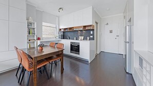 A modern kitchen with white cabinetry, a dining table with chairs, and a built-in oven. - Centennial Park Light Filled Modern Studio (Centennial Park)