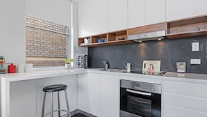 A modern kitchen with white cabinets, a black countertop, a brick backsplash, and a stainless steel oven. - Centennial Park Light Filled Modern Studio (Centennial Park)