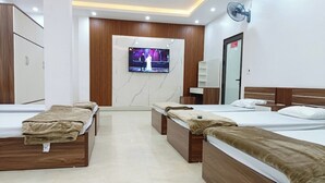 Une chambre d’hôtel avec quatre lits, un téléviseur fixé au mur, un ventilateur et un miroir.