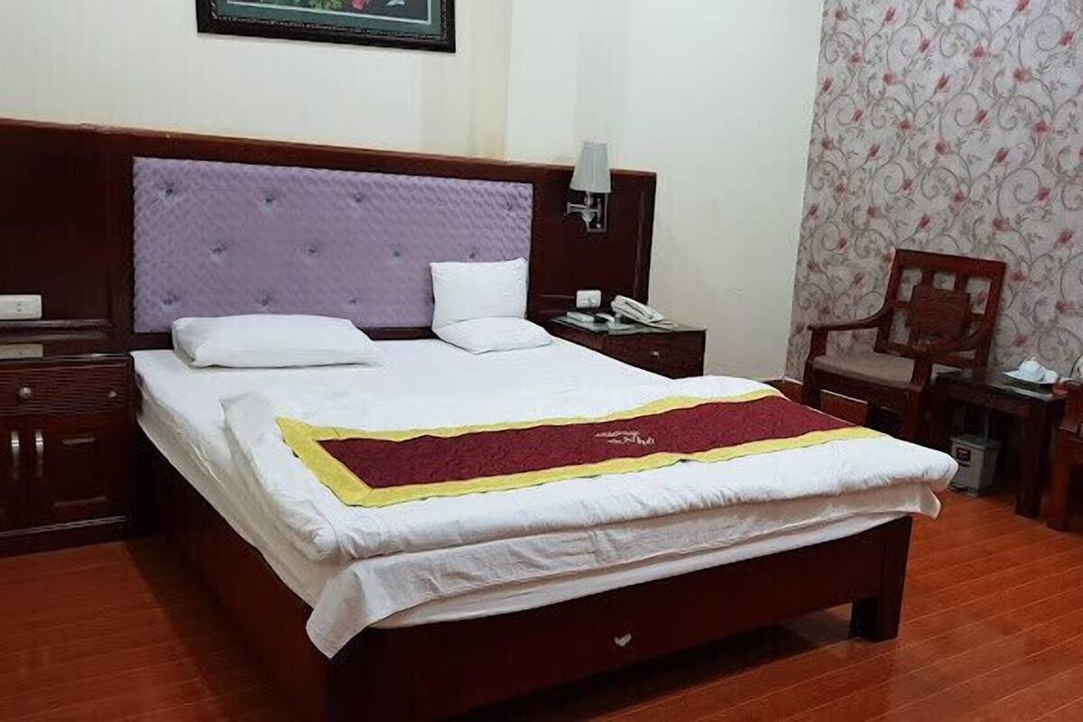 Habitación de hotel con una cama grande, una mesita de noche, un escritorio, dos sillas, una lámpara y un papel tapiz con estampado floral.