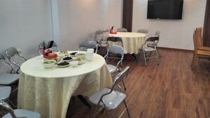 Une salle de conférence équipée de deux tables rondes, chacune entourée de chaises en métal. Un téléviseur à écran plat est fixé au mur.