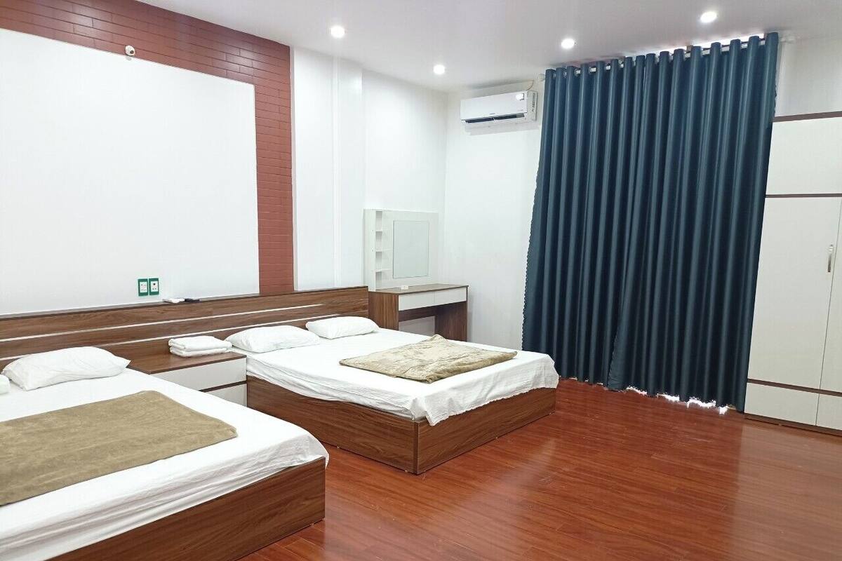 Habitación de hotel con dos camas de madera, un espejo grande, un equipo de aire acondicionado y una cortina azul.