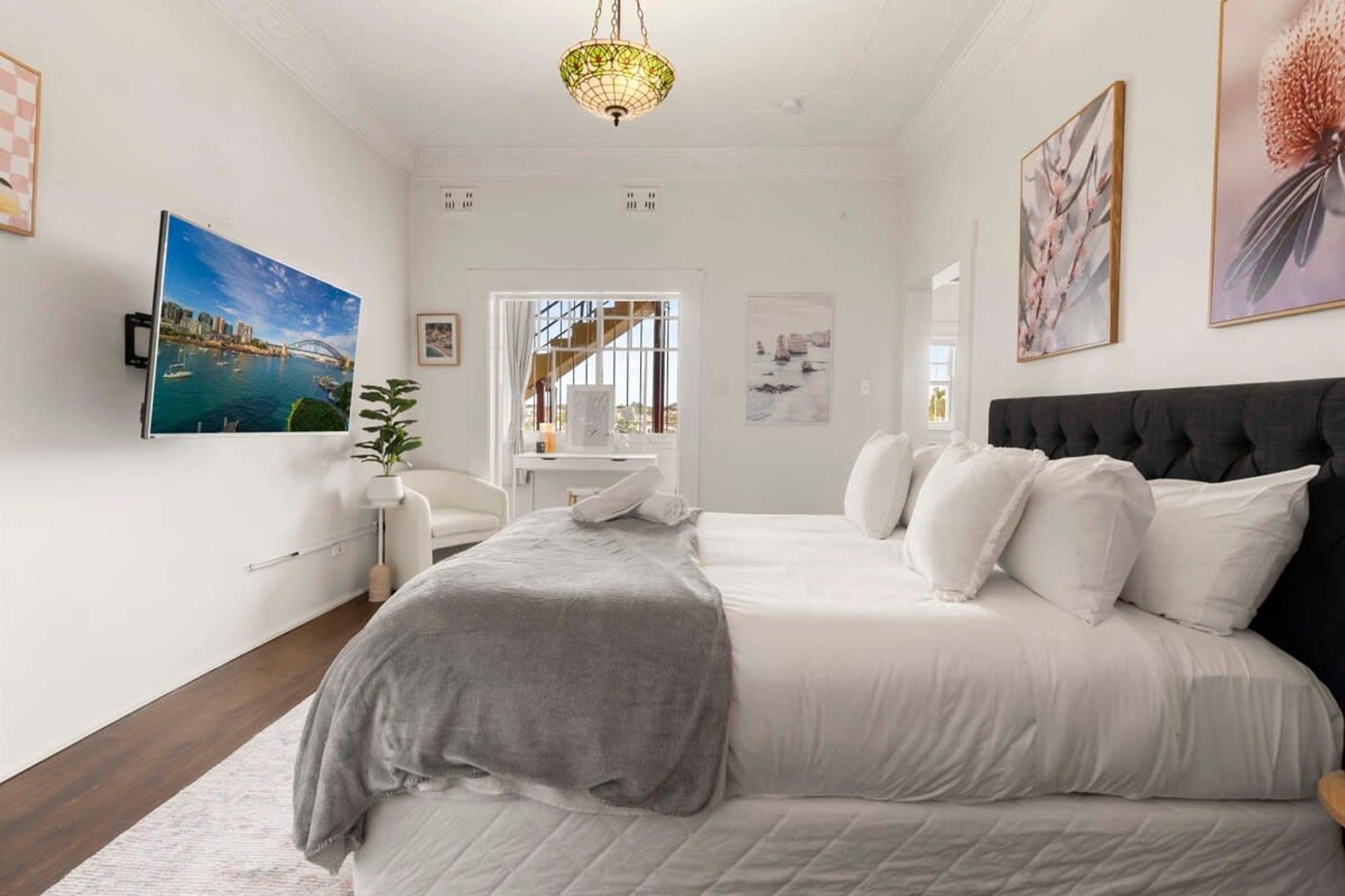 Un dormitorio con una cama grande, un escritorio y una silla. Hay cuadros en las paredes y una ventana con cortinas.