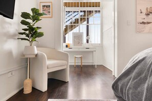 A modern room with a white armchair, a small desk, a potted plant, and artwork on the walls.