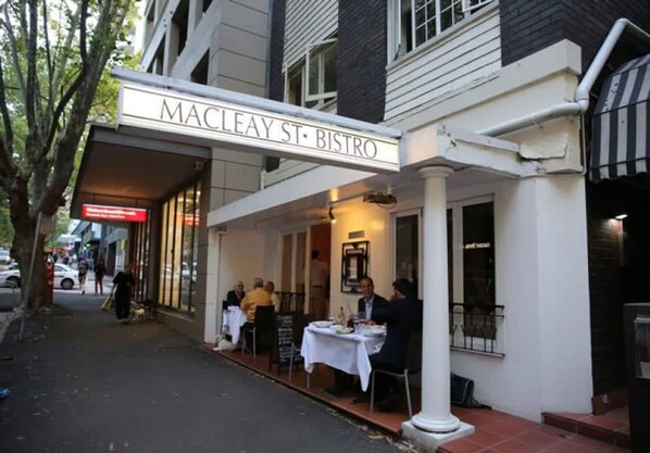 A bistro with outdoor seating, a covered entrance, and a street sign above.