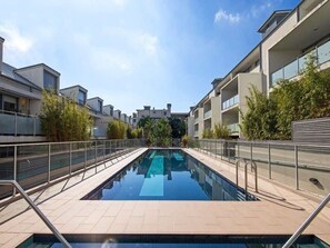 A modern pool area with a clear view of the pool, surrounded by apartment buildings and greenery.