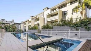 A modern residential building with a swimming pool, balconies, and a wooden deck. - Poolside Apartment Opposite Redfern Park (Redfern)