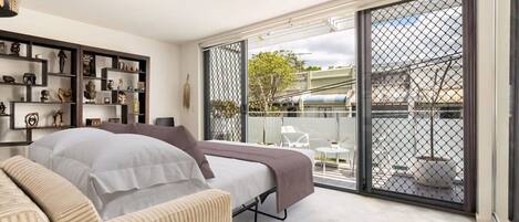 A modern bedroom with a bed, a sofa, and a balcony with a view of the city.