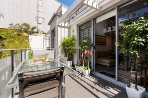 A modern outdoor patio with a glass table, seating, and potted plants.
