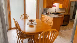 Een eethoek met een houten tafel en stoelen, een keuken met houten kasten, en een schuifdeur die leidt naar een terras.