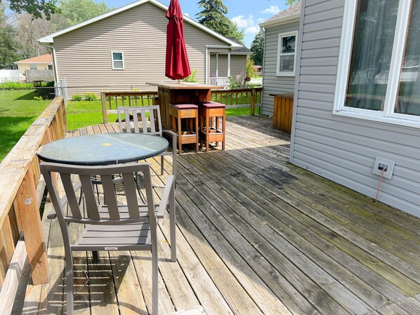 Une terrasse en bois avec une table et des chaises, un parasol rouge et une maison en arrière-plan.