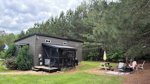A small cabin with a porch, a picnic table, and outdoor seating.