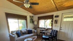 A spacious living room with a wooden ceiling, a ceiling fan, a sofa, a coffee table, and a dining area with a chair and table.