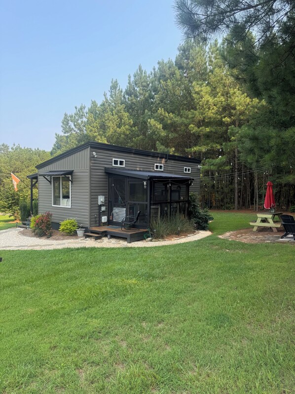 Eine moderne Holzhütte mit einer Terrasse, umgeben von einem gepflegten Rasen und dichtem Baumbestand.