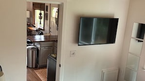 A bedroom with a bed, a television mounted on the wall, and a view into the kitchen area.