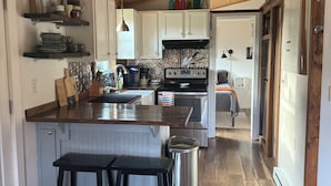 A modern kitchen with wooden ceiling, white cabinets, stainless steel appliances, and a central island with stools.
