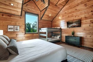 Een gezellig houten slaapkamer met stapelbedden, een groot raam en uitzicht op bomen.