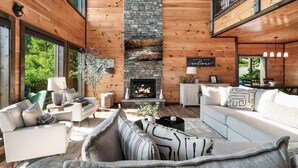 A cozy living room with a fireplace, wooden walls, and a balcony.