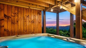 A hot tub with a wooden interior and a view of a sunset over mountains.