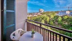 A balcony with a table and chairs, a potted plant, and a view of buildings and greenery. - Xaloc , Apartamento con Piscina y Junto la Playa (Na Macaret (Urbanitzacio))
