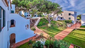 A residential area with white buildings, a tree-lined pathway, and a small staircase leading to a building entrance. - Xaloc , Apartamento con Piscina y Junto la Playa (Na Macaret (Urbanitzacio))