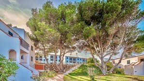 A pathway leading to a building with a stone wall and a blue building in the background. - Xaloc , Apartamento con Piscina y Junto la Playa (Na Macaret (Urbanitzacio))