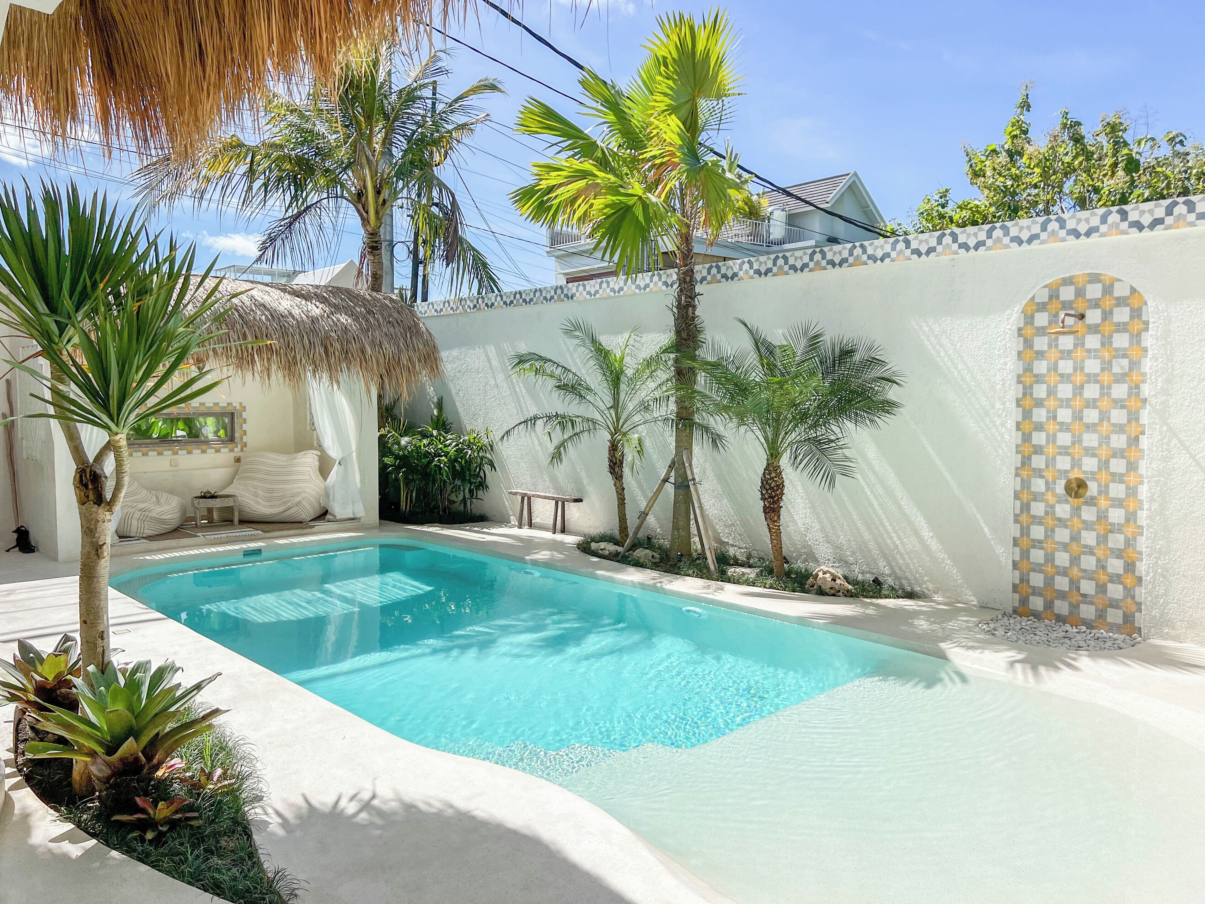 A swimming pool surrounded by palm trees and a thatched-roof structure.