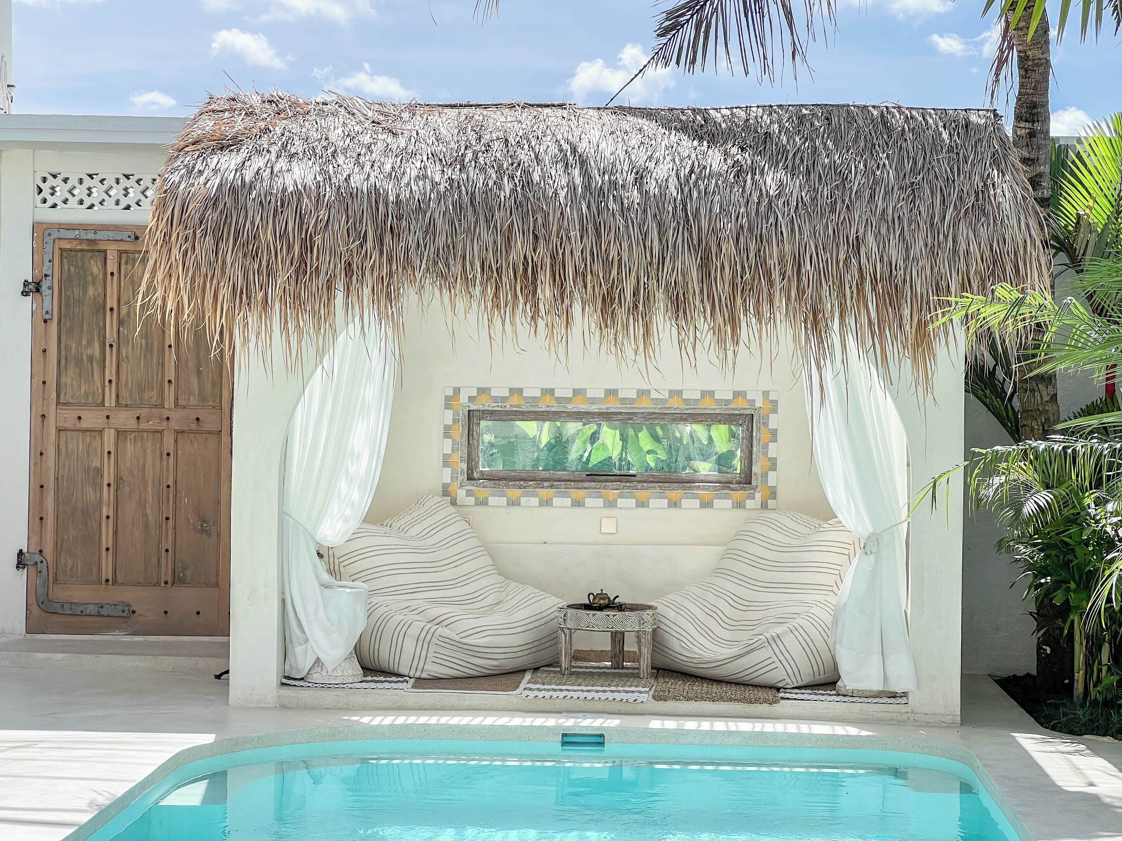 A pool area with a thatched roof structure, a wooden door, and a framed picture on the wall.