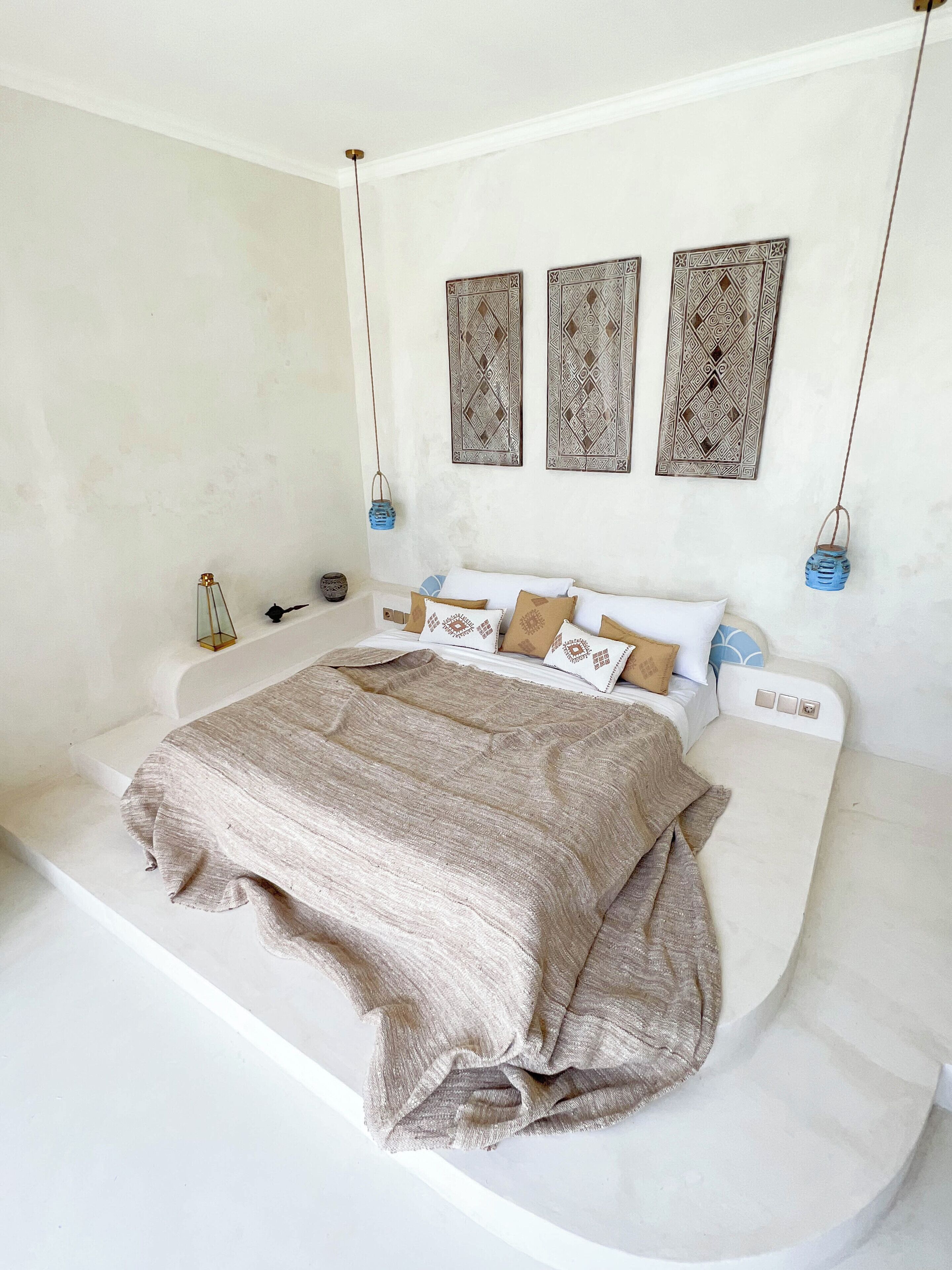 A modern bedroom with a large bed, a white wall, and three decorative wall hangings.