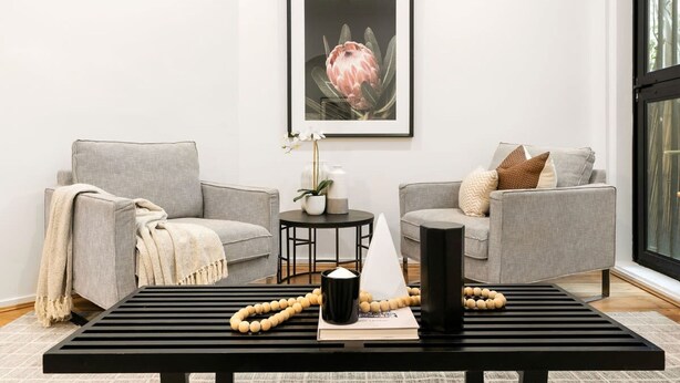 A modern living room with two grey sofas, a black coffee table, a framed artwork of a flower, and a small side table with a vase and decorative items. - Comfy Darlinghurst Retreat (Darlinghurst)