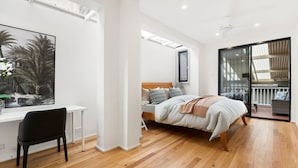 A modern bedroom with a wooden floor, a bed with a headboard, a desk with a chair, and a large window. - Comfy Darlinghurst Retreat (Darlinghurst)