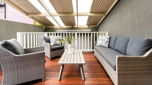 A covered patio with wicker furniture, a white table, and a grey sofa. - Comfy Darlinghurst Retreat (Darlinghurst)