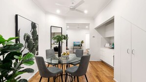 A modern dining area with a glass table, grey chairs, and a ceiling fan. - Comfy Darlinghurst Retreat (Darlinghurst)