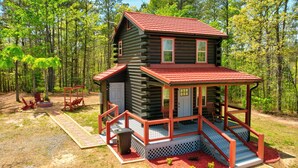 Une cabane en rondins à deux étages, dotée d’un porche et entourée d’une forêt.