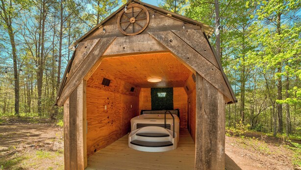 Une cabane en bois avec un jacuzzi à l’intérieur, entourée d’une forêt.
