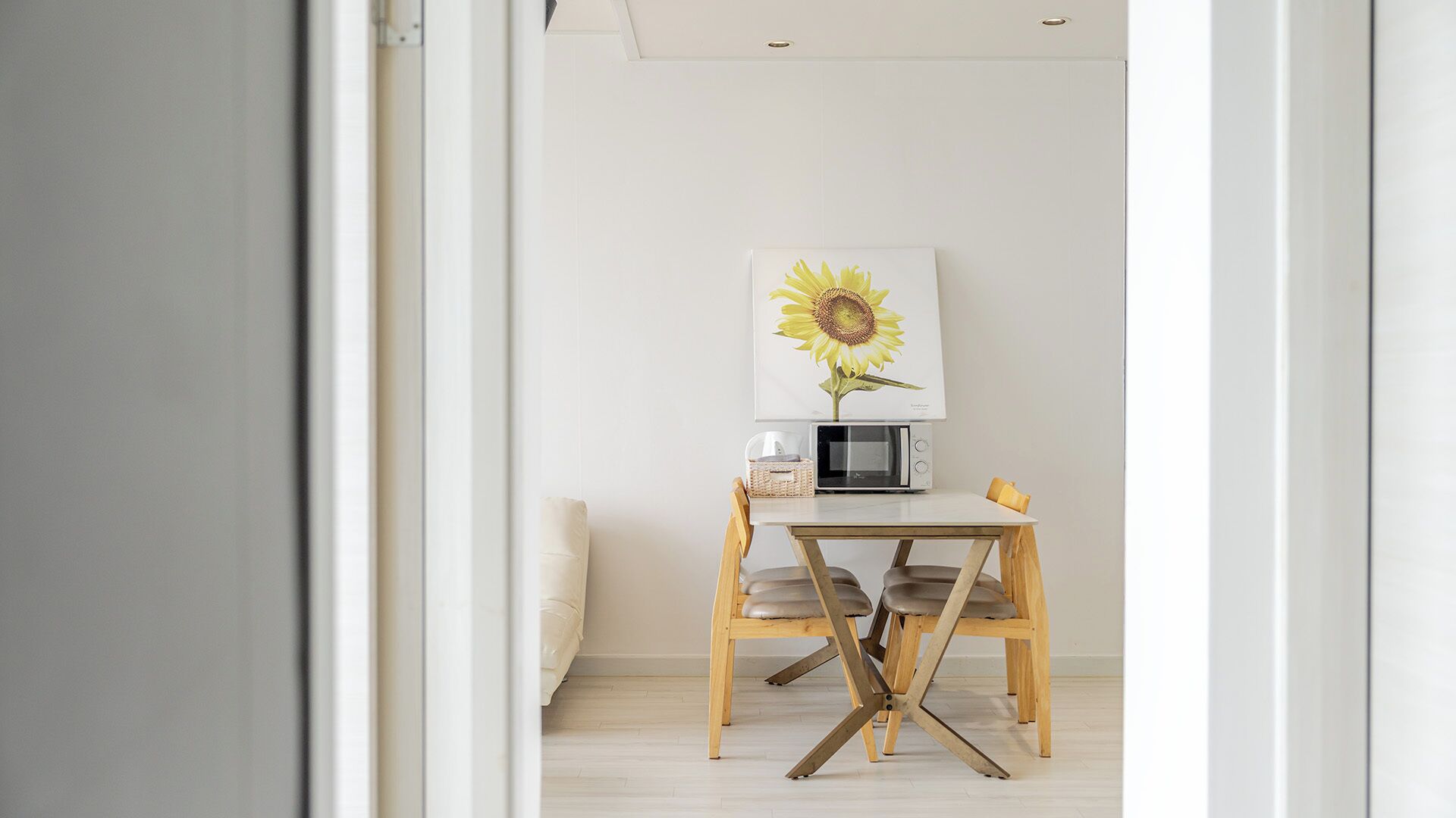 Een kamer met een houten tafel, een magnetron en een lijst met een zonnebloem erop.