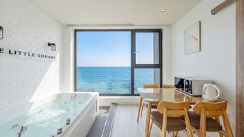 Una habitación con bañera, una mesa con sillas, un hervidor de agua y vista al mar.