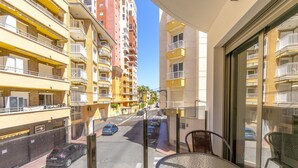 Un balcon avec une table et des chaises, donnant sur une rue animée où l’on peut voir des voitures et des immeubles.