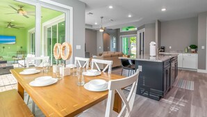 Una cucina moderna con isola centrale, un'area pranzo con tavolo in legno e un soggiorno con divano e poltrone.