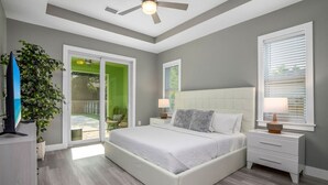Una camera da letto con un letto grande, una ventola a soffitto, un comodino, una TV e una porta vetrata scorrevole che dà su un patio.