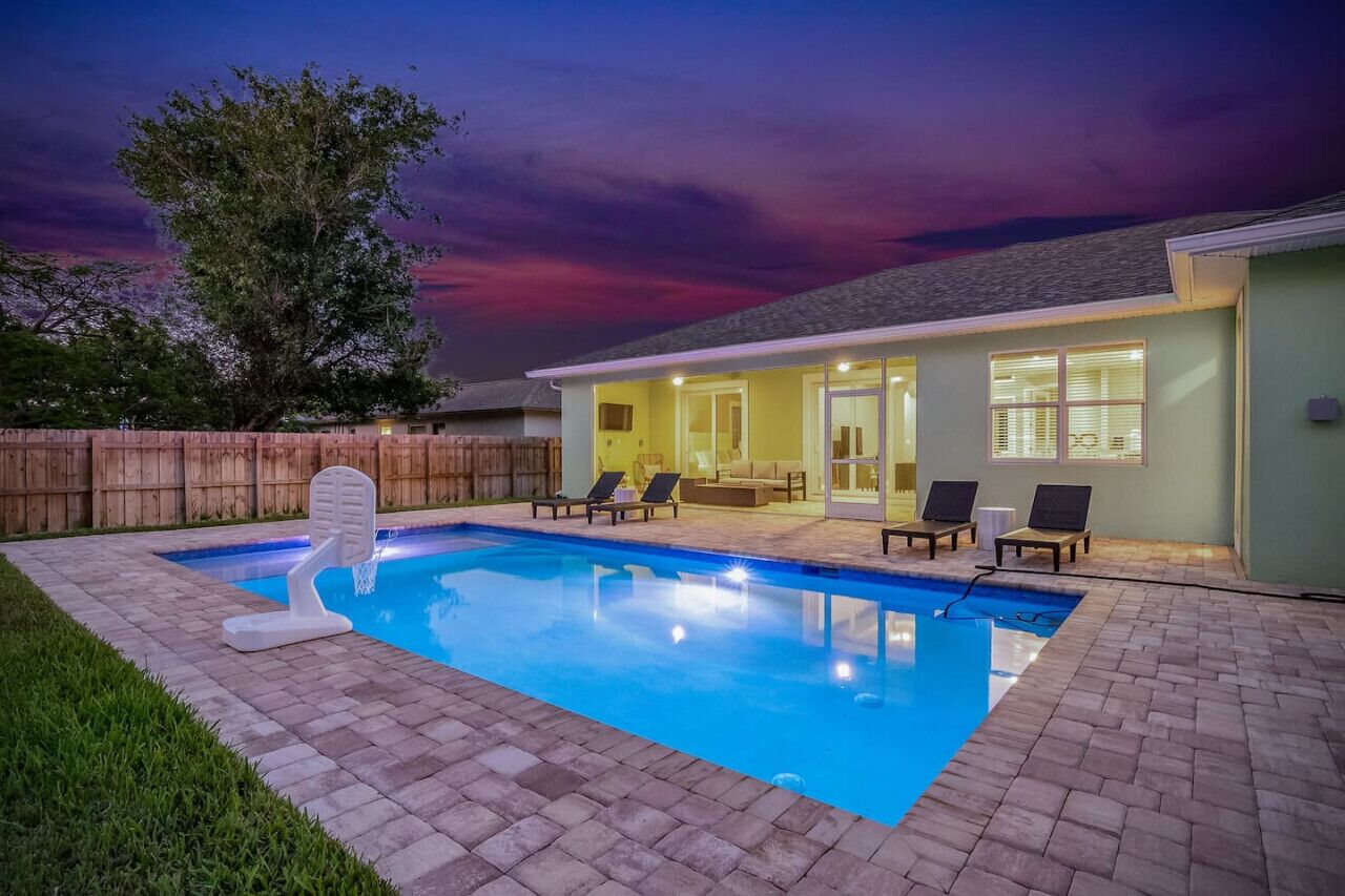 Un jardin avec une piscine, une clôture en bois et une maison dotée d’un patio couvert.