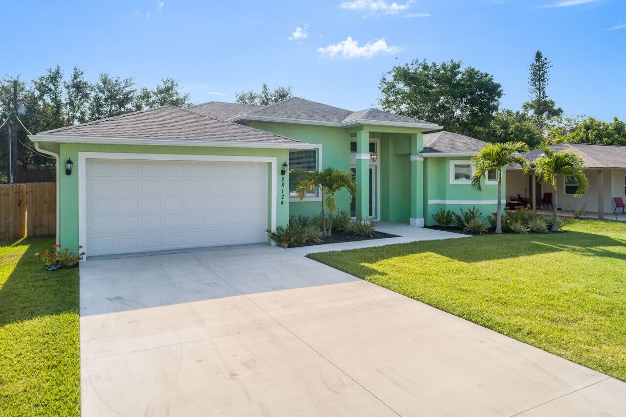 A two-story house with a green exterior, a white garage door, and a driveway leading to the front door.
