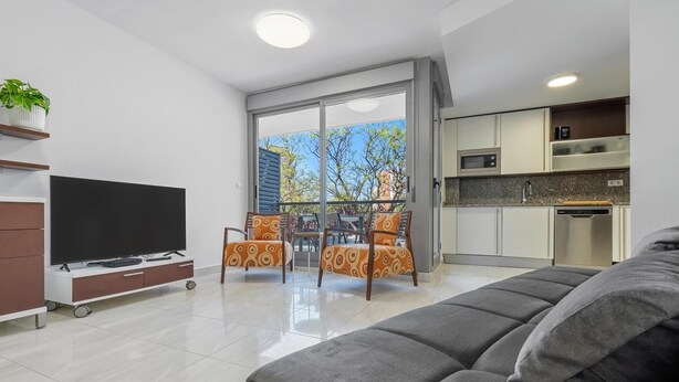 A modern living room with a flat-screen TV, a sofa, and a dining area with patterned chairs. - Apartment with pool and parking 350m beach (Cambrils)
