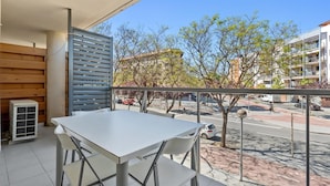 A balcony with a white table and chairs, overlooking a street with trees and buildings. - Apartment with pool and parking 350m beach (Cambrils)